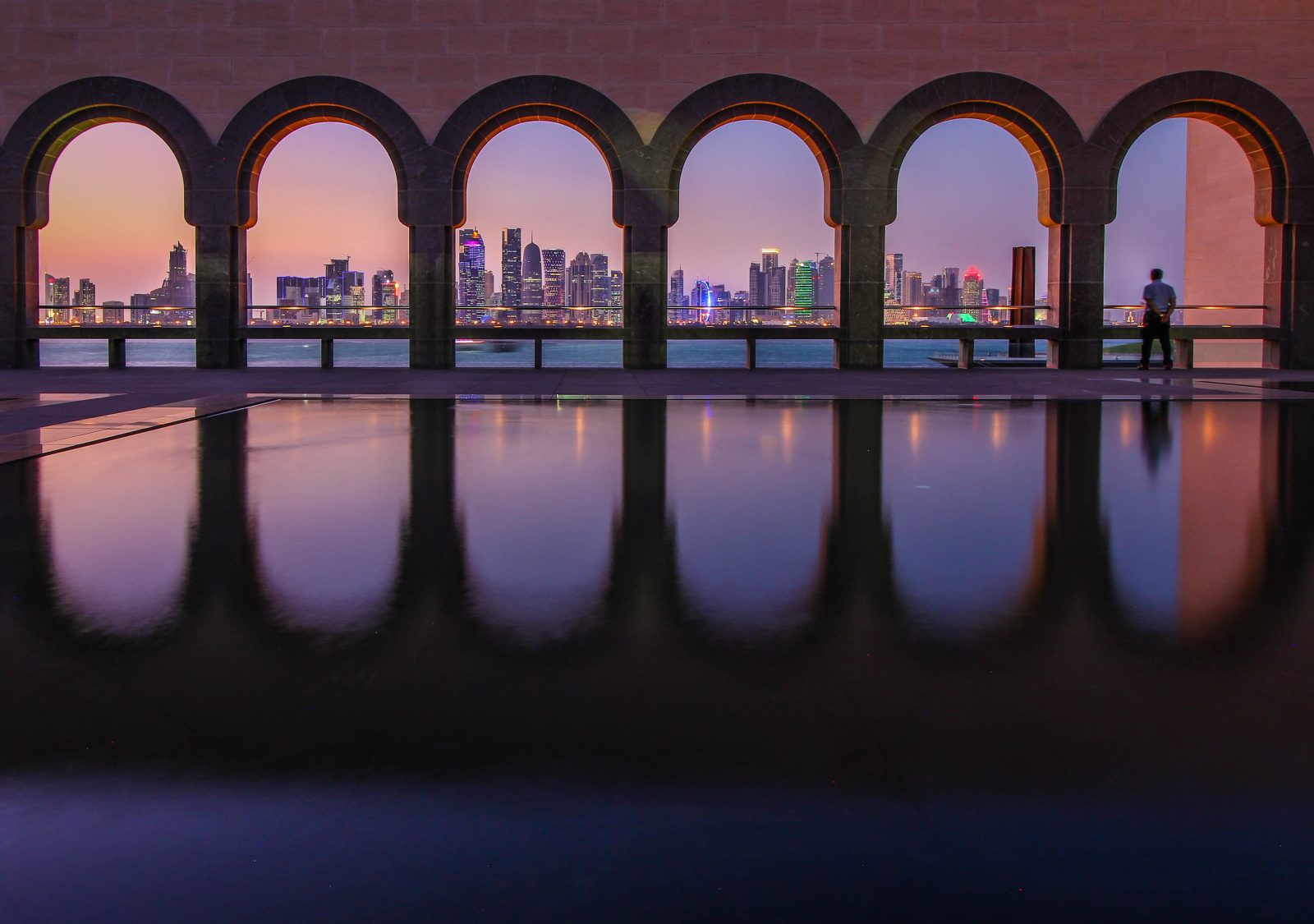 a pool with arches and a city skyline in the distance