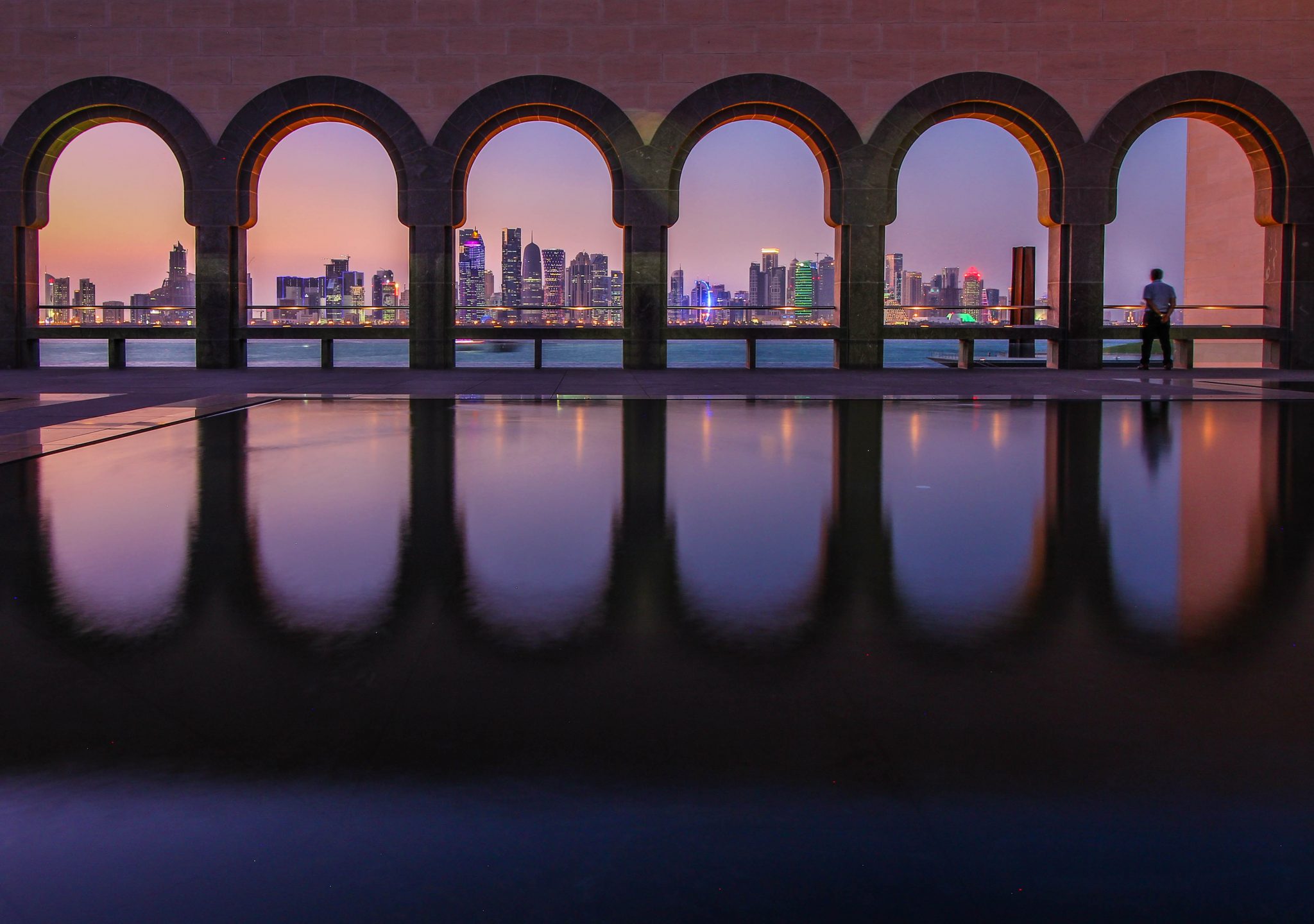 a pool with arches and a city skyline in the distance
