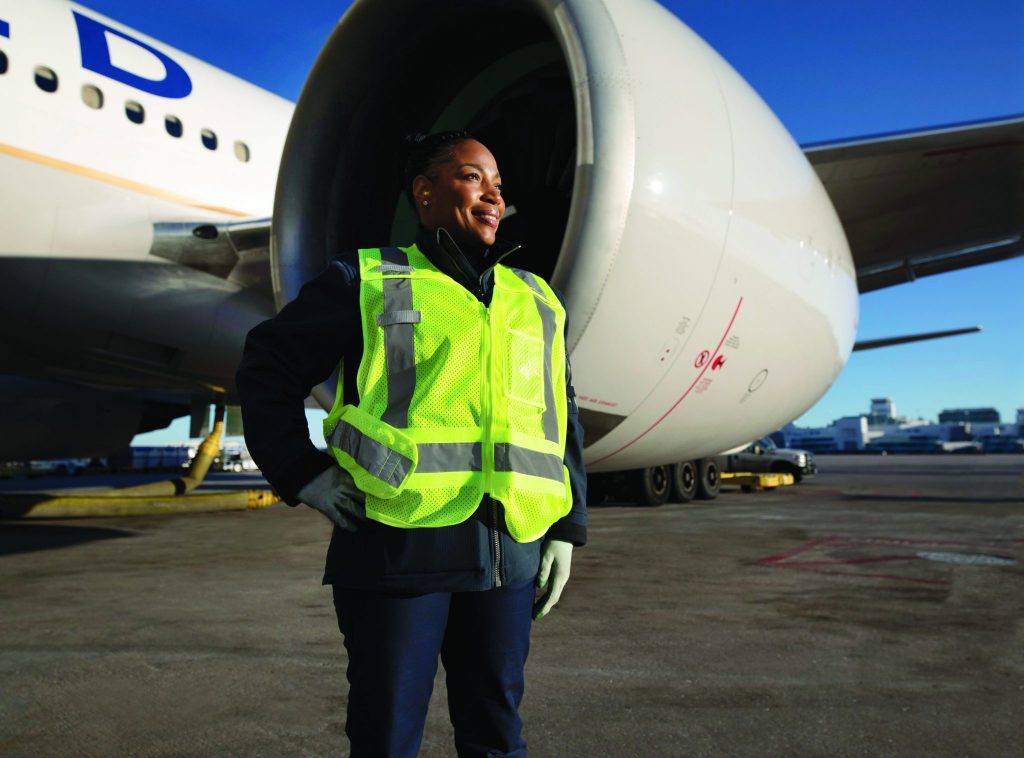 a woman wearing a safety vest standing in front of an airplane