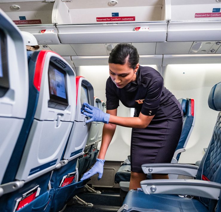 a woman in a uniform and gloves touching an airplane seat
