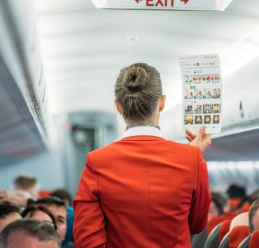 flight attendant holding up safety card in front of passengers
