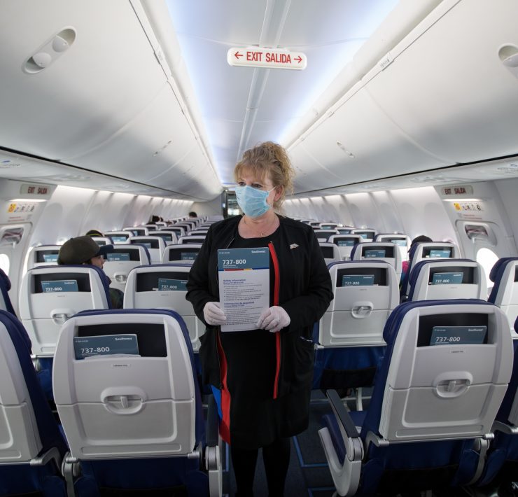 a woman wearing a mask holding a sign in an airplane