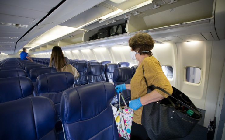 a woman in a mask and gloves carrying luggage on an airplane