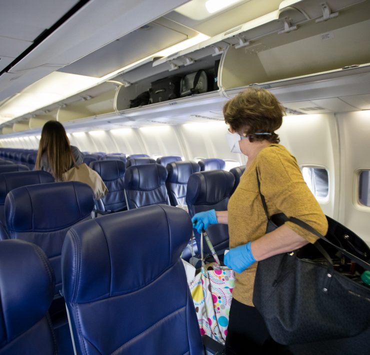 a woman in a mask and gloves carrying luggage on an airplane