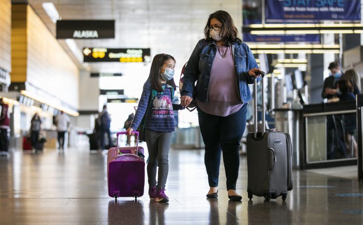 a woman and a girl wearing face masks walking with luggage
