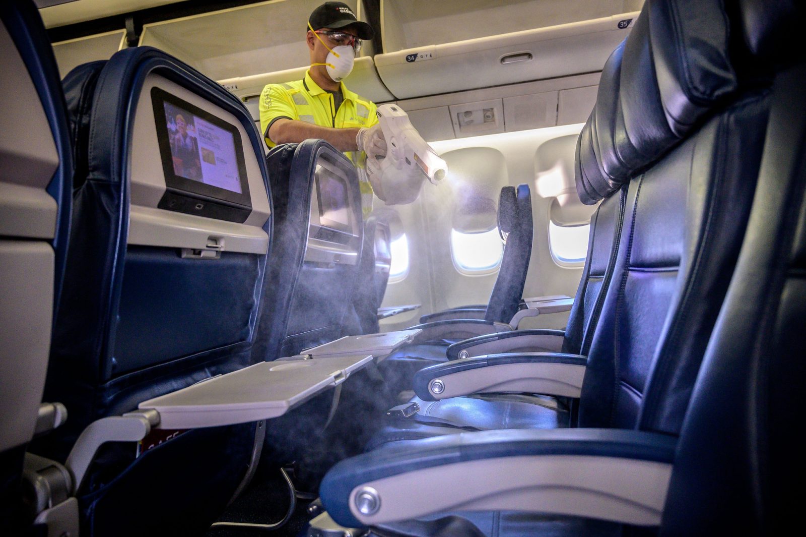 a man wearing a mask and gloves spraying a table in an airplane