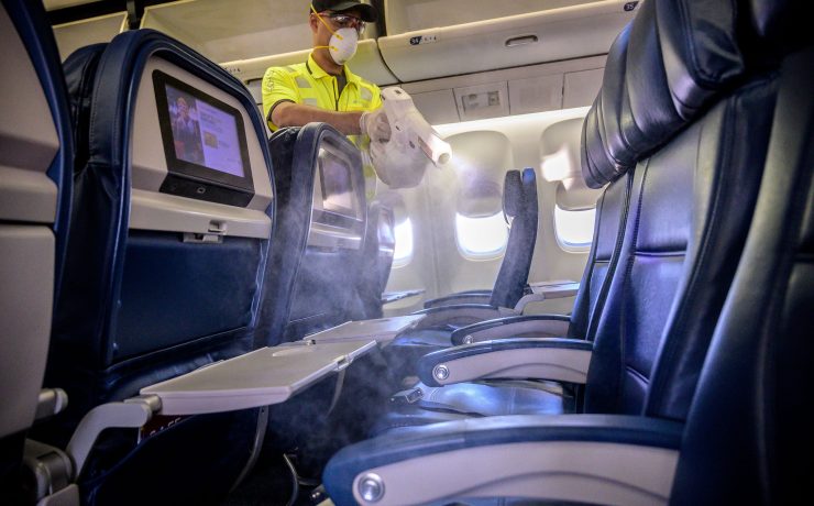 a man wearing a mask and gloves spraying a table in an airplane