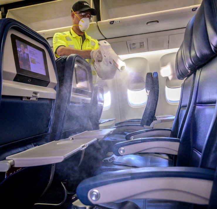 a man wearing a mask and gloves spraying a table in an airplane