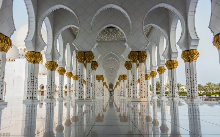 a large white and gold building with columns with Sheikh Zayed Mosque in the background