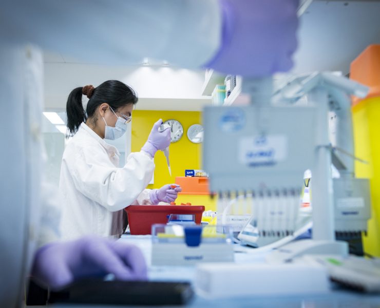 a woman in a lab coat and mask holding a dropper