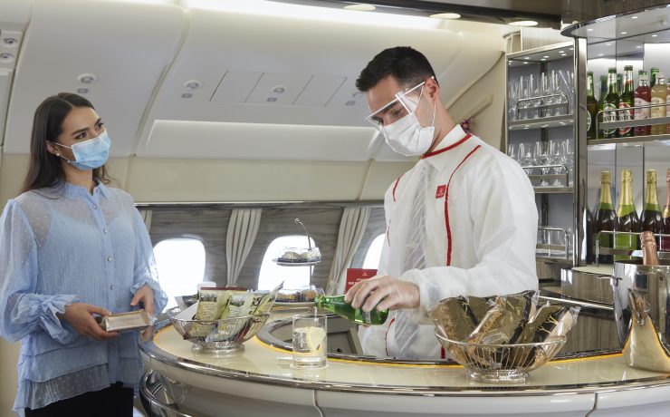 a man wearing face mask and white coat standing at a counter in an airplane