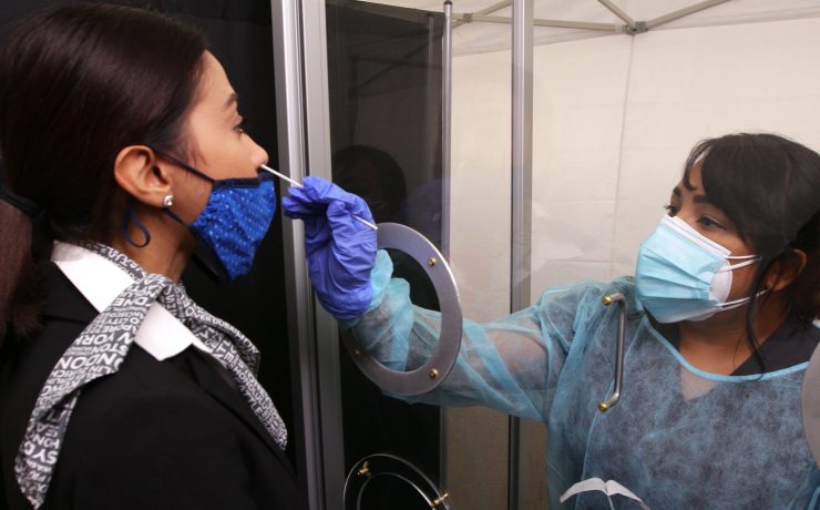 a woman wearing a mask and gloves holding a needle to a woman's face