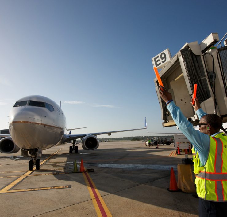 a man in a safety vest holding an object in front of an airplane