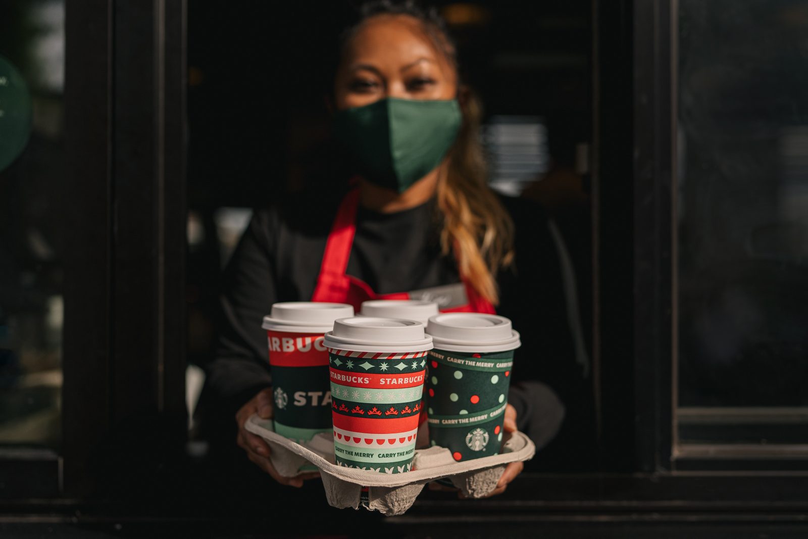 a woman wearing a face mask holding a tray of coffee cups