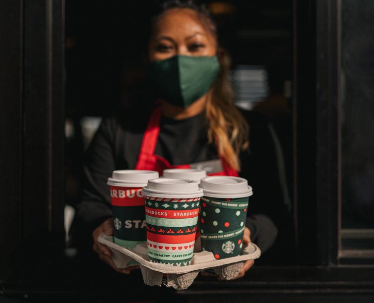a woman wearing a face mask holding a tray of coffee cups