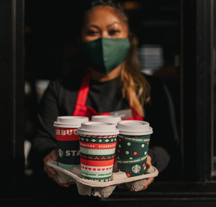 a woman wearing a face mask holding a tray of coffee cups