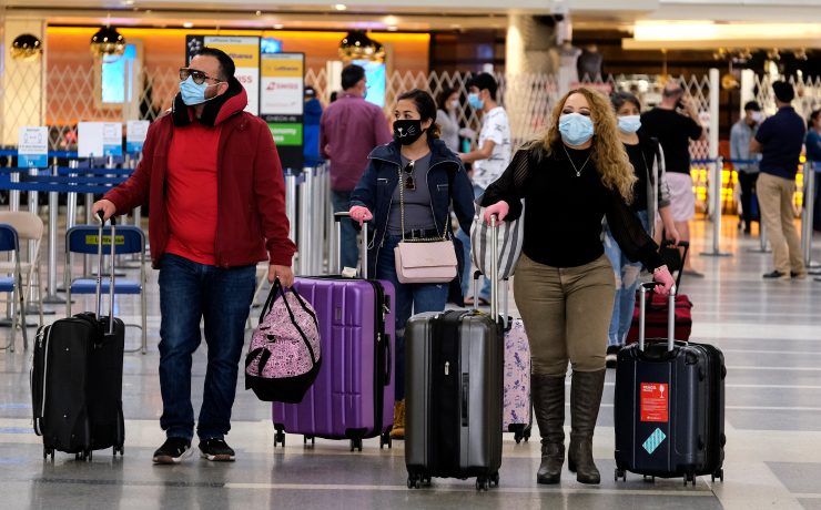 a group of people wearing face masks walking with luggage