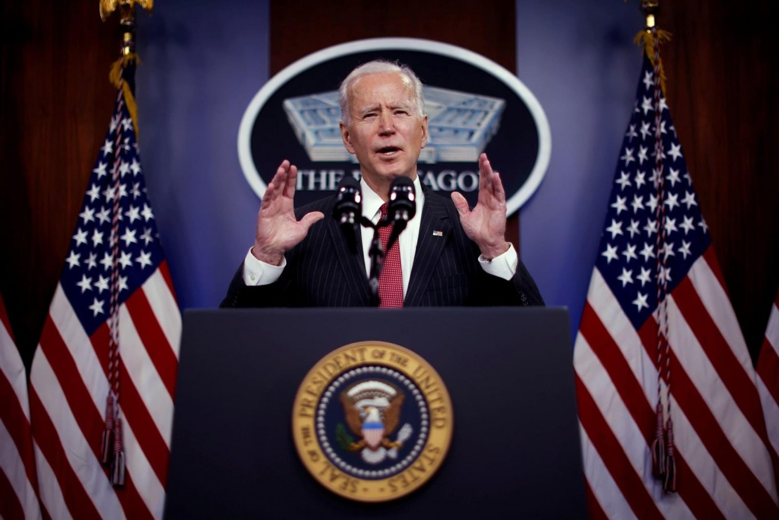 a man standing at a podium with flags behind him