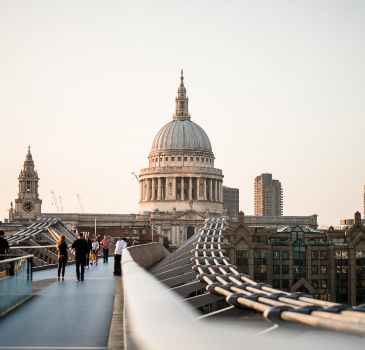 a group of people walking on a bridge with a dome and a building in the background