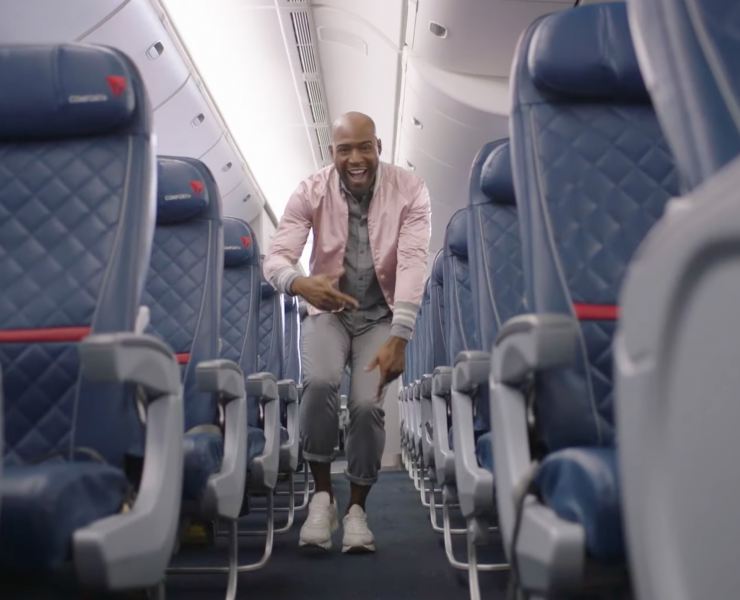 a man in a pink jacket and grey pants laughing in an airplane