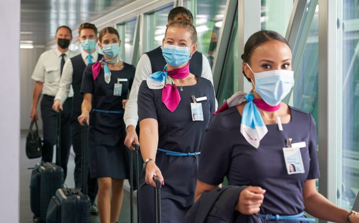 a group of people wearing masks and walking with luggage