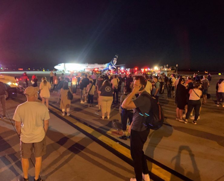 passengers walk on the tarmac next to an Alaska Airlines Boeing 737 after evacuating via emergency slides