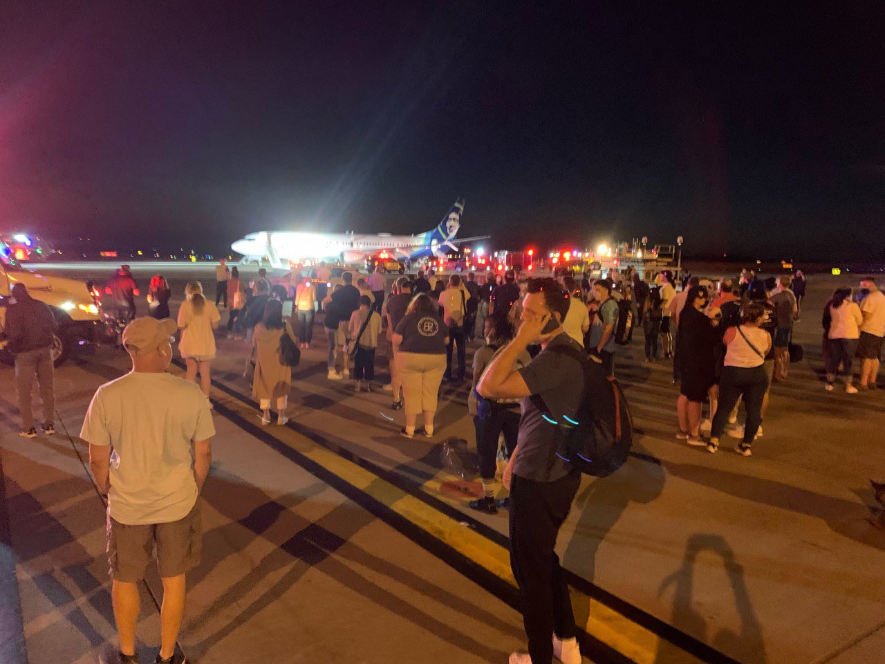 passengers walk on the tarmac next to an Alaska Airlines Boeing 737 after evacuating via emergency slides