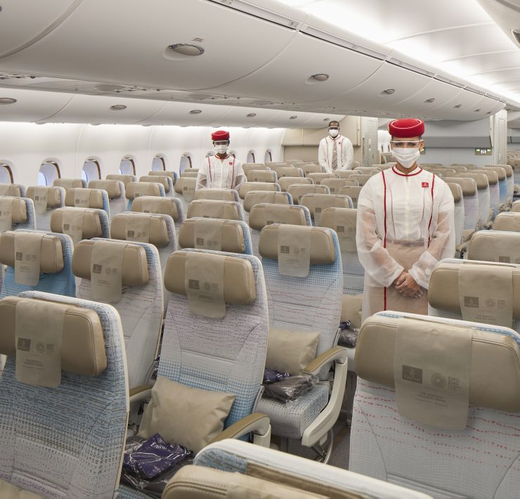 people in a plane with people wearing masks and standing in the middle of seats