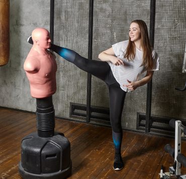 woman kicking a bob self defense training mannequin in a gym