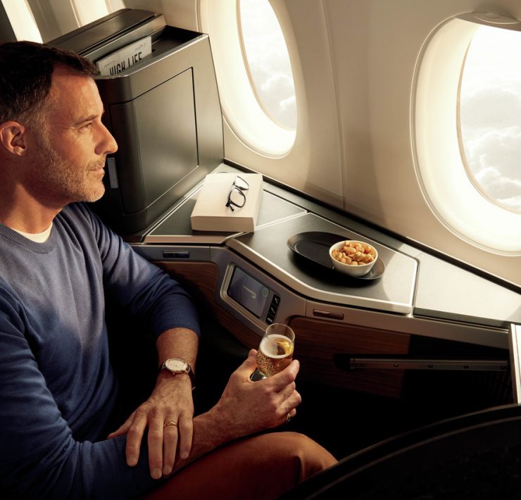 a man sitting in an airplane with a drink and a bowl of food