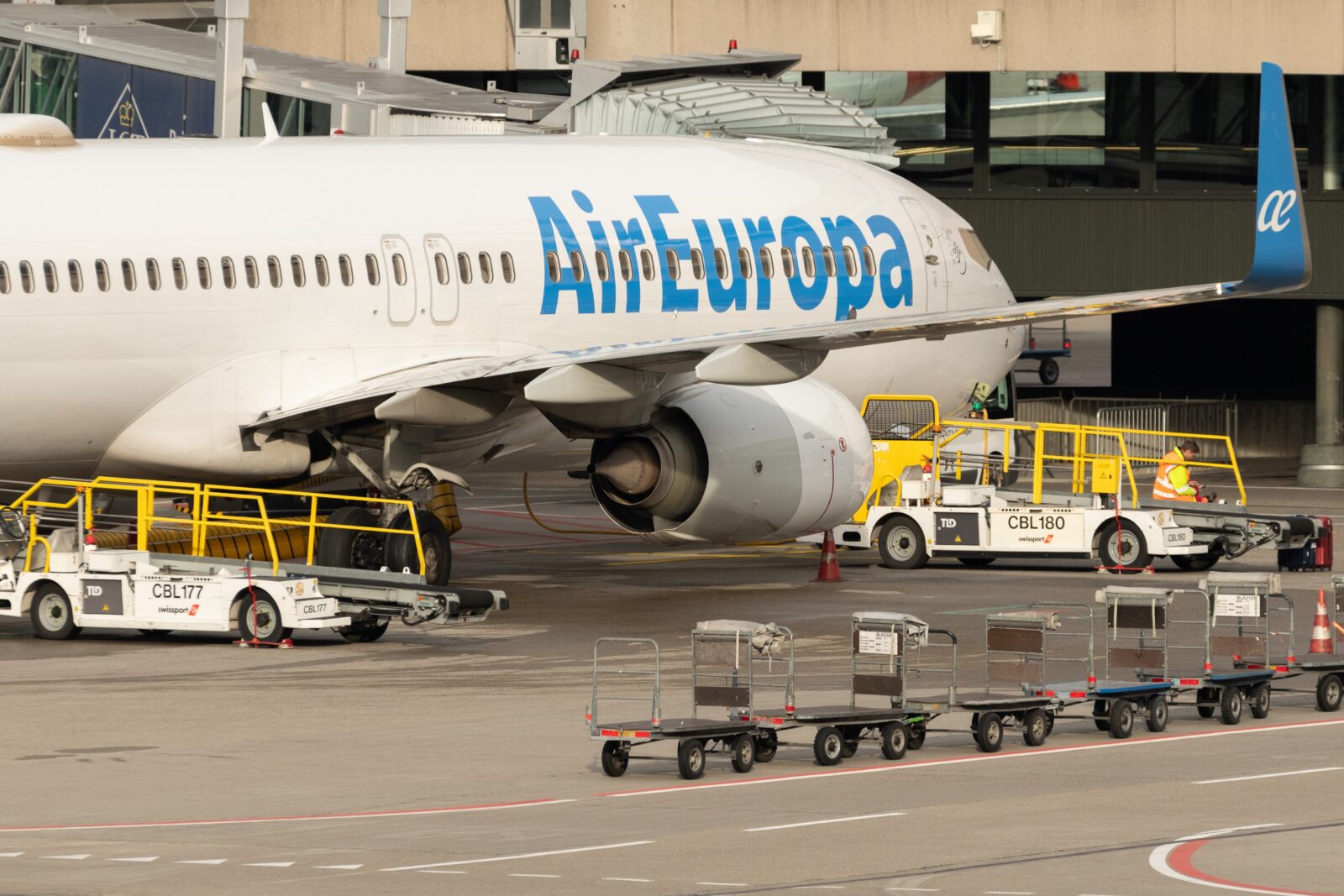 a large airplane with luggage carts and a building