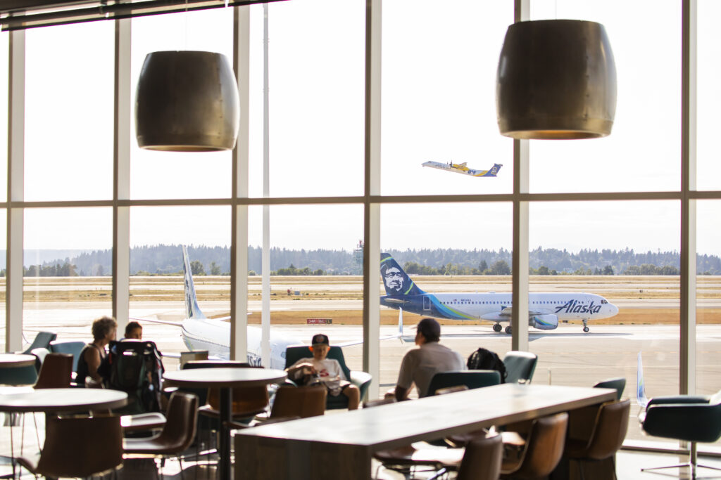 people sitting at tables in a room with a plane in the background