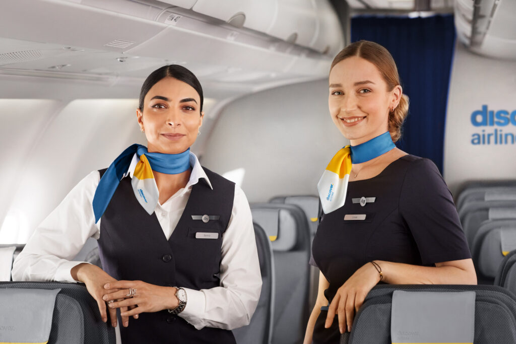 two women wearing uniforms and standing in an airplane