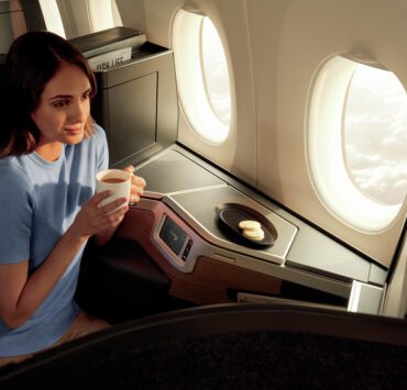 a woman sitting in an airplane with a cup of coffee and cookies