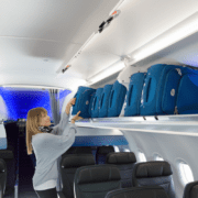 a woman standing in an airplane with luggage on shelves