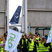 a group of people in yellow vests holding signs and a plane in the background