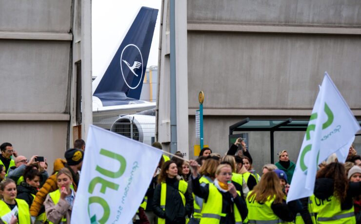 a group of people in yellow vests holding signs and a plane in the background