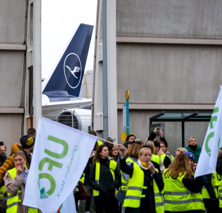 a group of people in yellow vests holding signs and a plane in the background