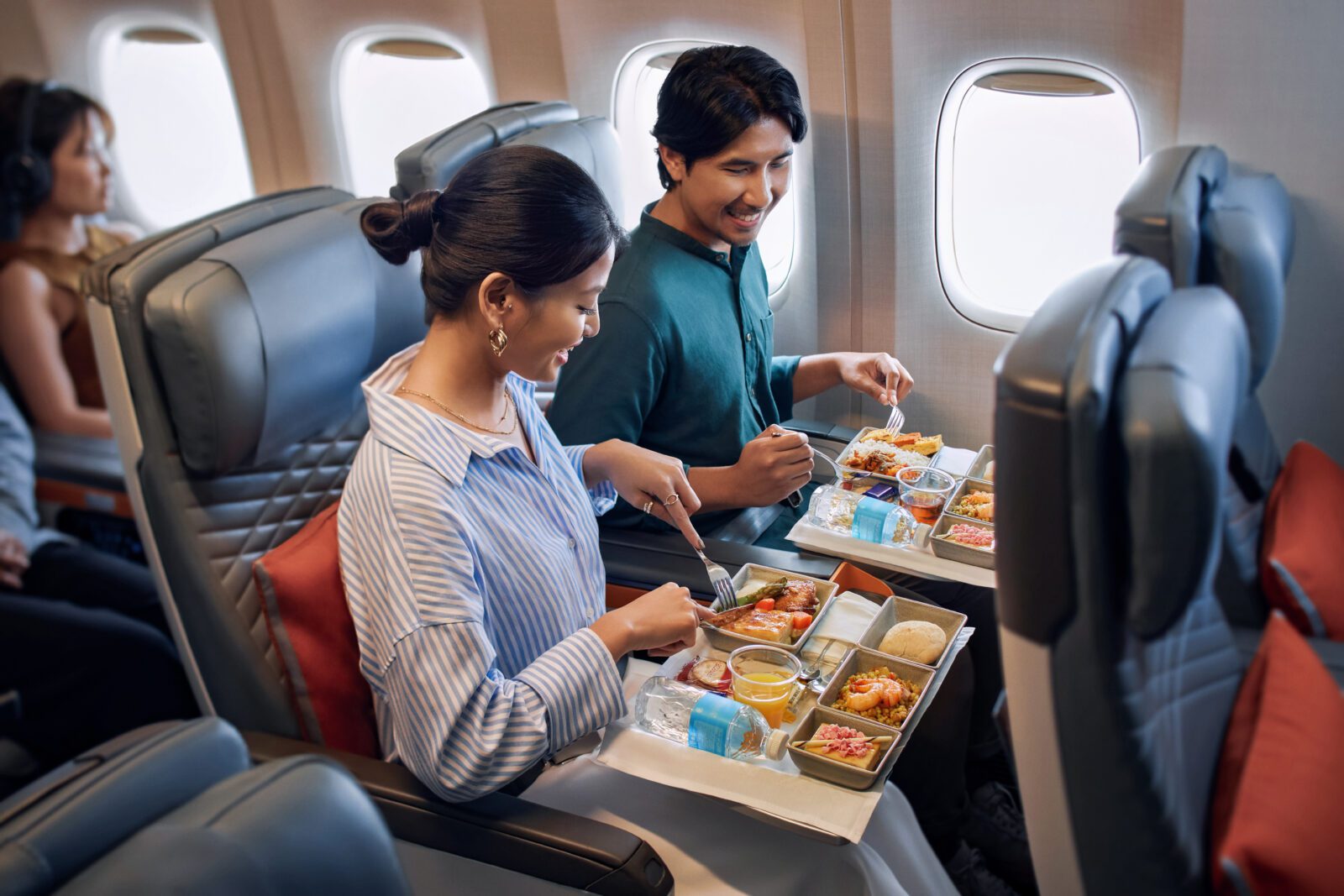 a man and woman eating food on an airplane