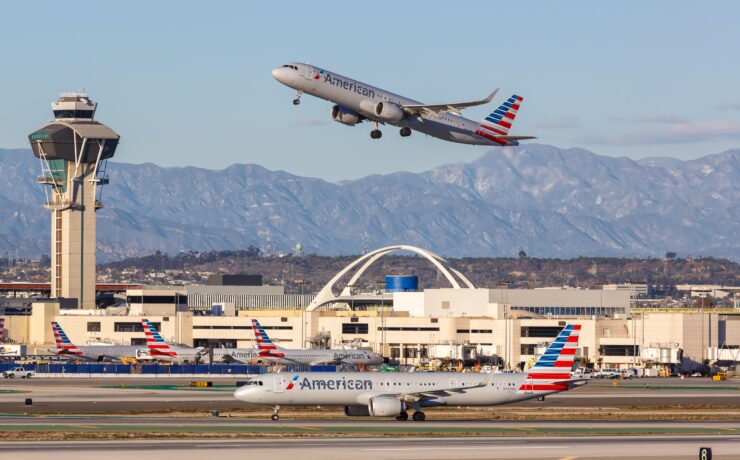 an airplane flying over a runway with buildings and mountains in the background