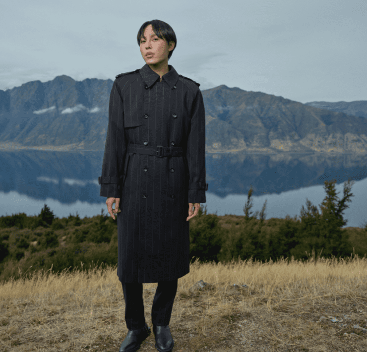 a man in a long trench coat standing in front of a lake