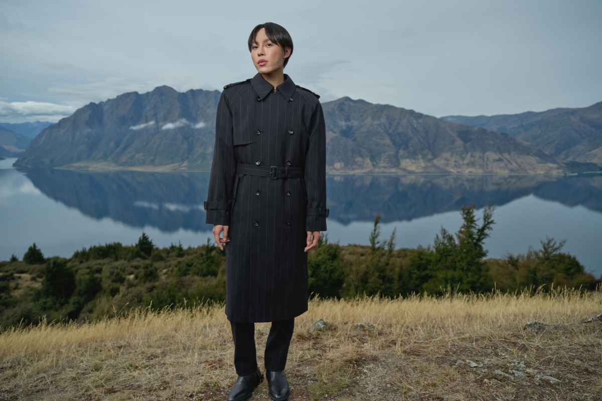 a man in a long trench coat standing in front of a lake