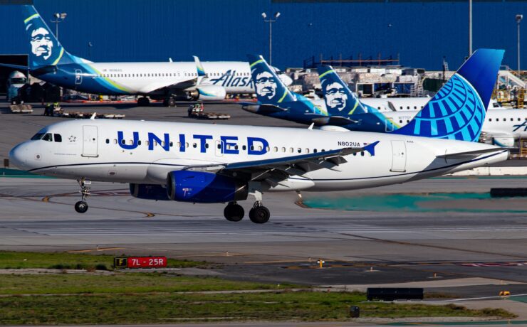 A united airlines airbus a319 landing in front of several Alaska Airlines airplanes