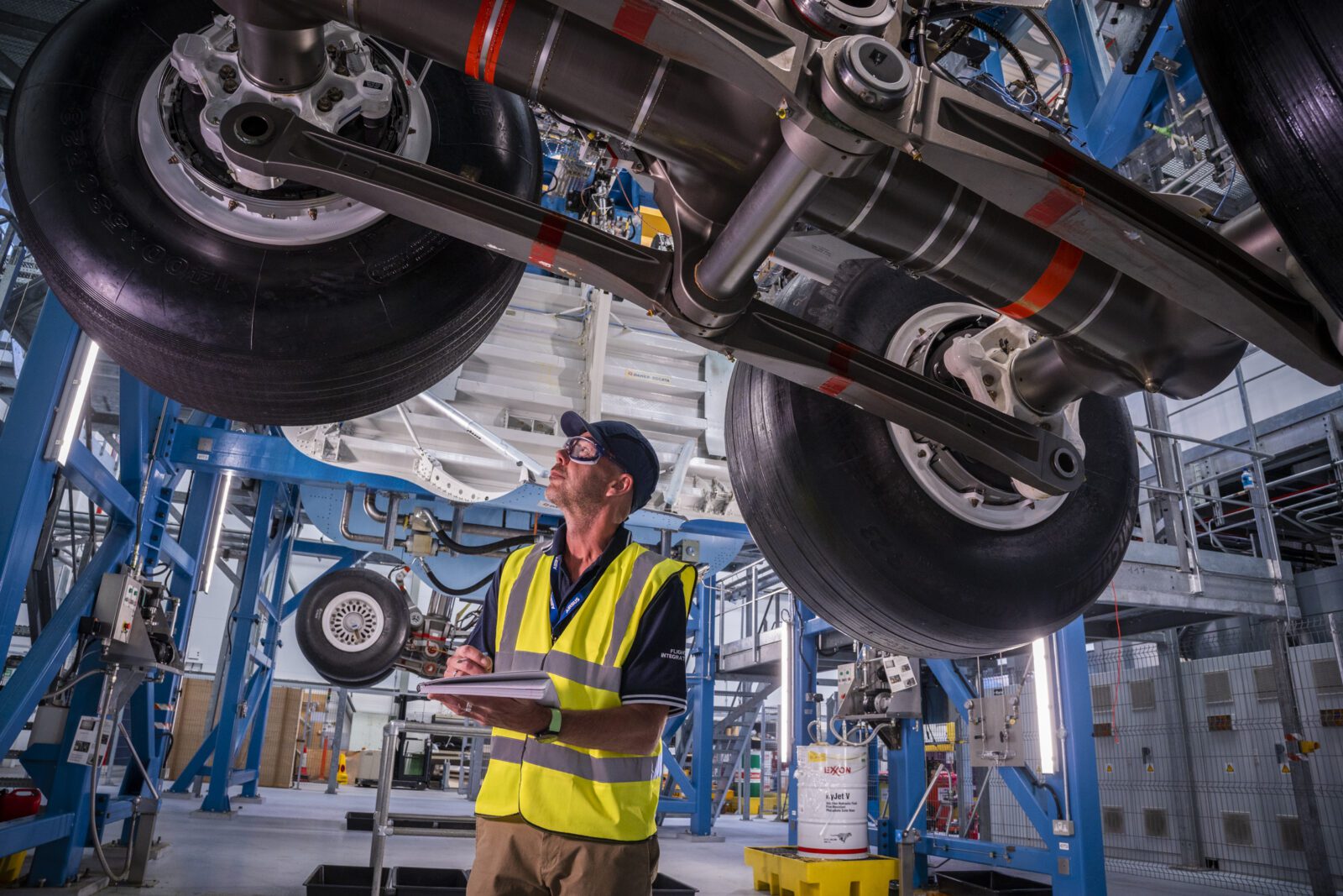 a man in a safety vest and hat standing under a large machine