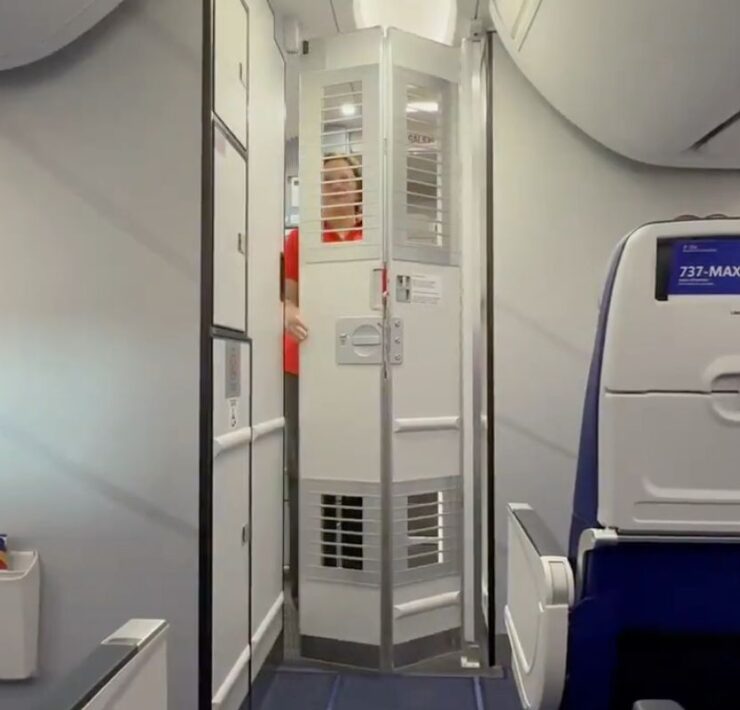 a southwest airlines flight attendants standing behind a partially open secondary cockpit door on a boeing 737max