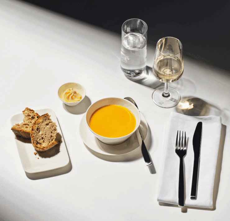 a bowl of soup and bread on a plate with a fork and knife