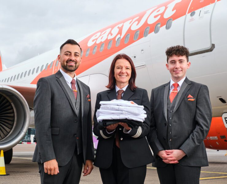 Two easyjet cabin crew and a pilot holding old uniforms in front of an airplane