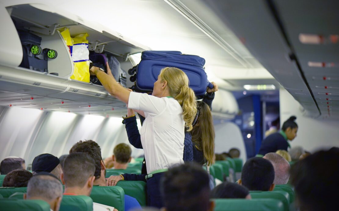 a flight attendant struggles to help a passenger stow their luggage in the overhead bin
