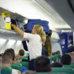 a flight attendant struggles to help a passenger stow their luggage in the overhead bin