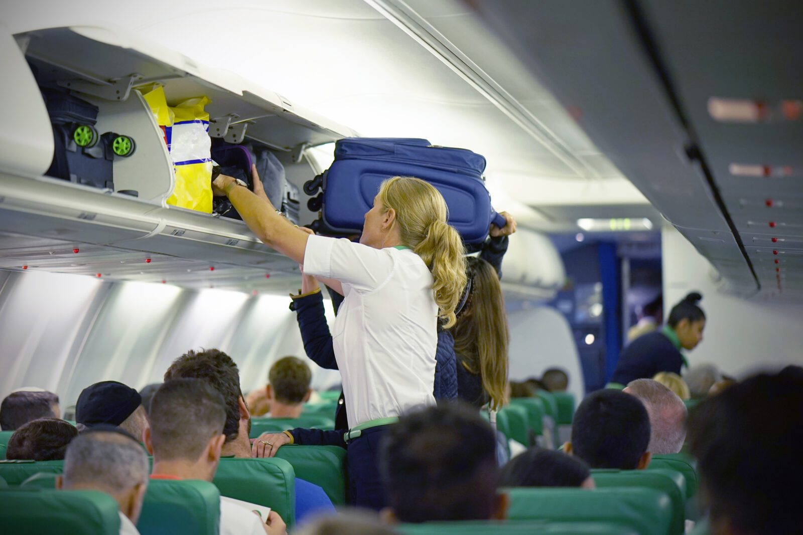 a flight attendant struggles to help a passenger stow their luggage in the overhead bin